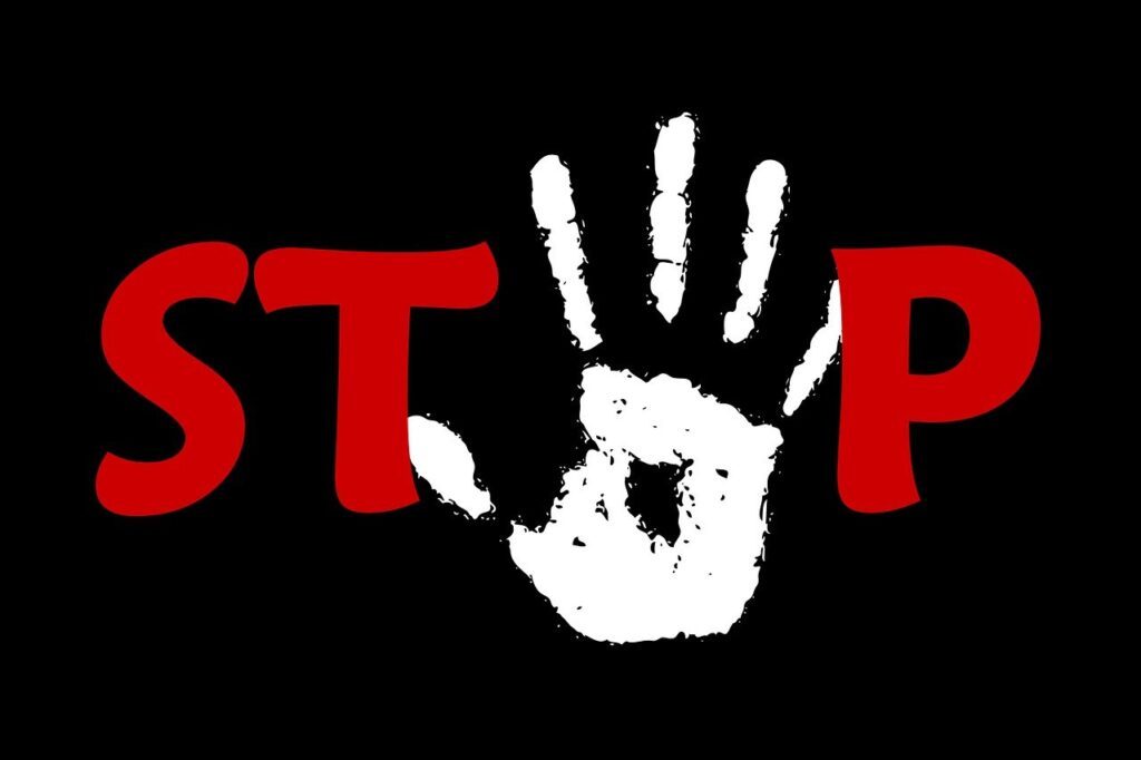 A Red STOP on a black background with a white painted handprint over the O of the STOP