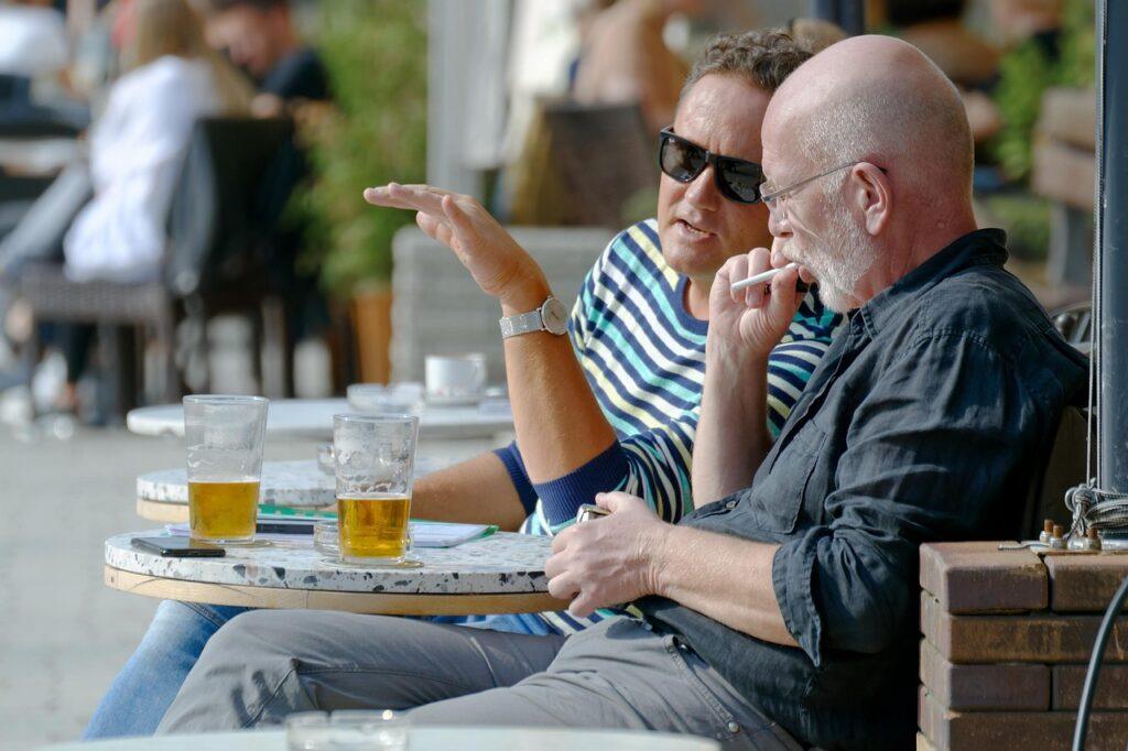 Two men sitting side by side at a bistro table with a beer, deep in conversation with each other, Talking as a Friend